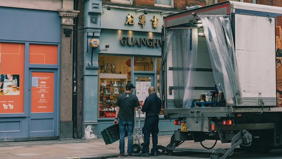 Two removal personnel from Camberwell Removals are preparing for a home relocation outside a shop with Chinese characters and the name